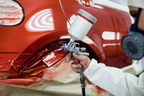 Man with protective clothes and mask painting car using spray compressor.