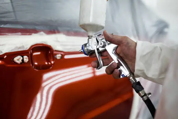 Man with protective clothes and mask painting car using spray compressor.