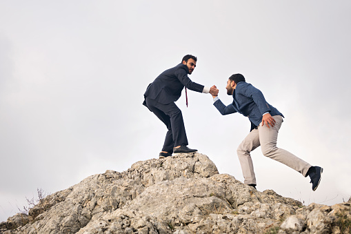 Businessman helping his business team member on mountain peak to reach success