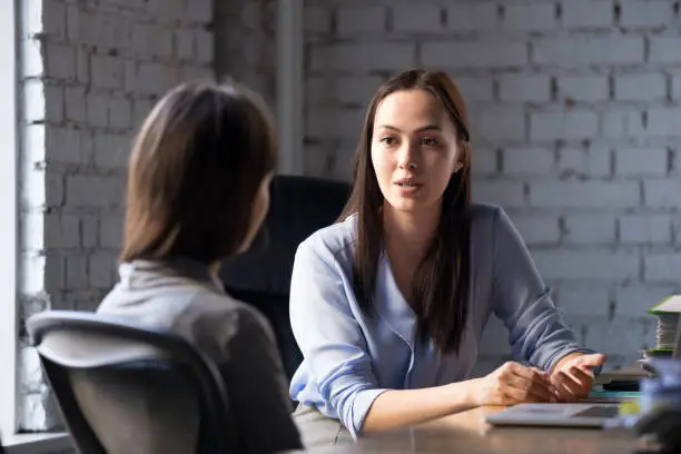 Serious professional female advisor consulting client at meeting talking having business conversation or making offer, insurer giving advice, mentor teaching intern, hr speaking at job interview