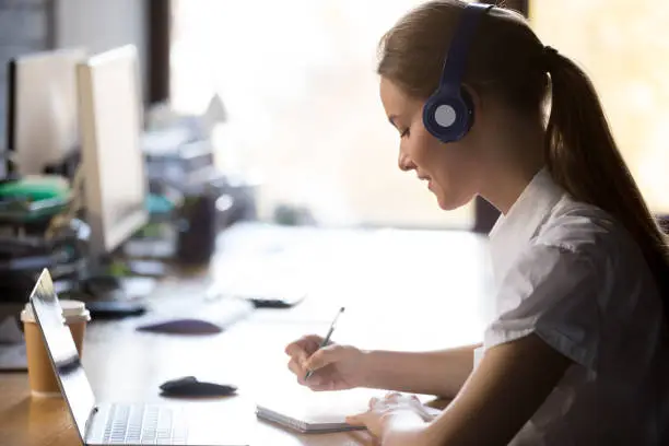 Photo of Focused woman wearing headphones write notes study online with teacher