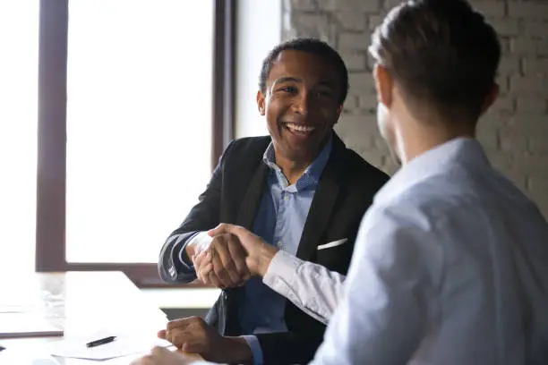 Photo of Satisfied black client shaking hands thanking manager for good deal