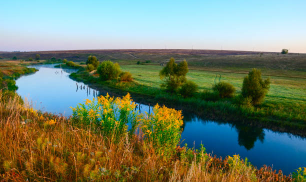 istock Sunny summer landscape with river flowing between the beautiful green hills,fields and meadows. 1085713976