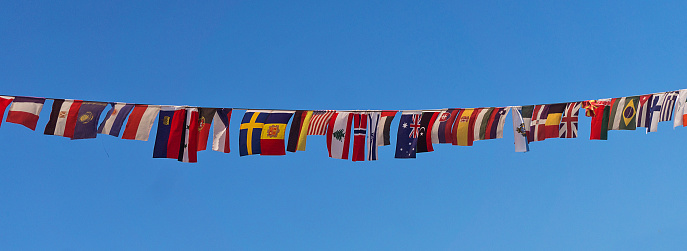 Row of small flags of different countries on a rope against a blue sky