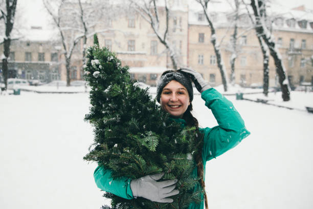 mulher andando na cidade com árvore de natal - christmas tree standing clothing adventure - fotografias e filmes do acervo