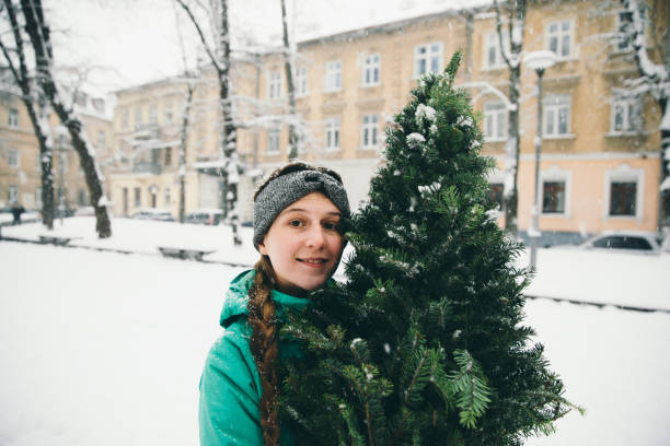 mulher andando na cidade com árvore de natal - christmas tree standing clothing adventure - fotografias e filmes do acervo