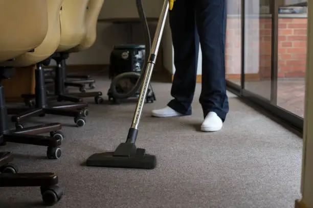 Photo of Man vacuuming the carpet of an office