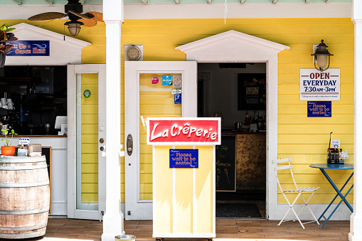 Key West, USA - May 1, 2018: La Creperie in Florida keys city on street, sidewalk with building, restaurant, cafe entrance, sign for open hours, please wait to be seated in yellow colorful color
