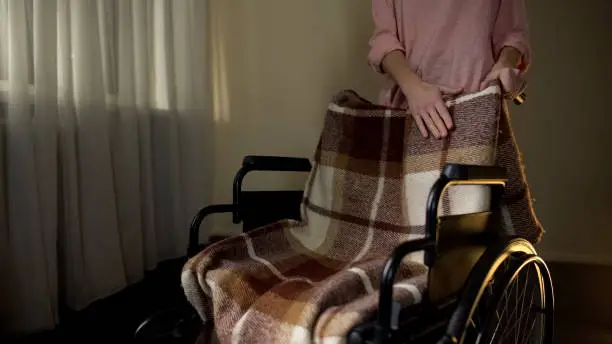 Daughter stroking empty wheelchair with sorrow, remembering mother passed away