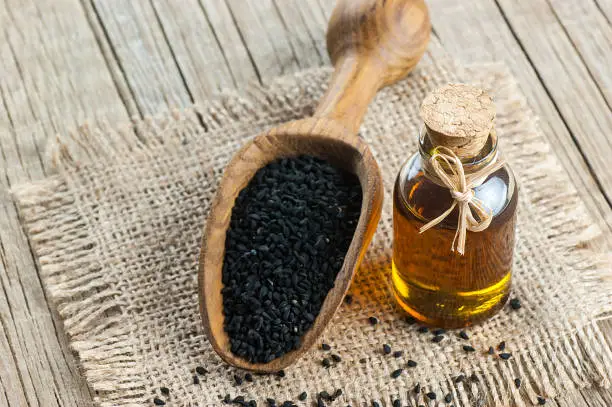 Black cumin seeds essential oil with wooden spoon or shovel on wooden background, Nigella Sativa in glass bottle. Organic herbal medicine for many diseases