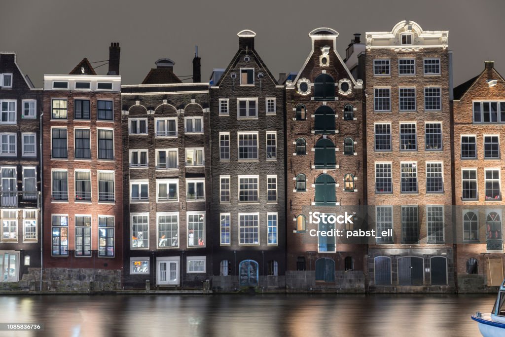Amsterdam skyline close-up buildings waterfront Damrak Set of neighboring buildings downtown Amsterdam, in front of a canal - Damrak. Night photograph with sightseeing boats. Amsterdam Stock Photo