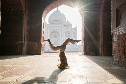 Young woman practicing yoga in India at the famous Taj Mahal at sunrise - Headstand position upside down- People travel spirituality zen like concept