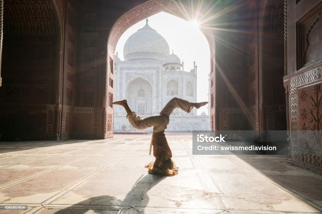 Young woman practicing yoga in India at the famous Taj Mahal at sunrise - Headstand position upside down- People travel spirituality zen like concept Yoga Stock Photo