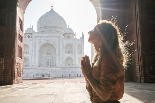 Young woman practicing yoga in India at the famous Taj Mahal at sunrise - prayer position hands to heart- People travel spirituality zen like concept