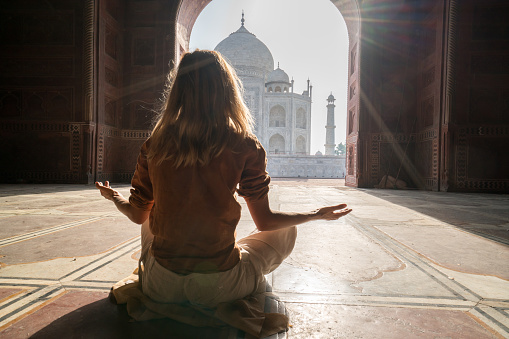 Young woman practicing yoga in India at the famous Taj Mahal at sunrise -  People travel spirituality zen like concept