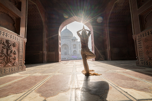 Young woman practicing yoga in India at the famous Taj Mahal at sunrise -  People travel spirituality zen like concept