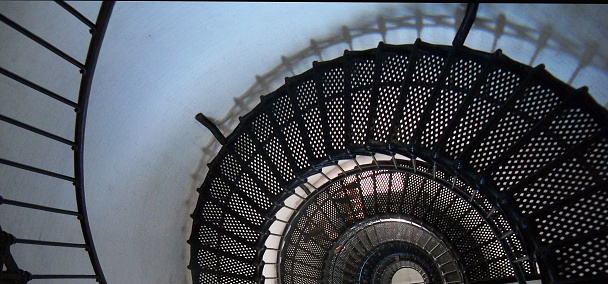 Looking upwards at black metal spiral staircase.  Looks industrial with an interesting circular and geometric pattern.