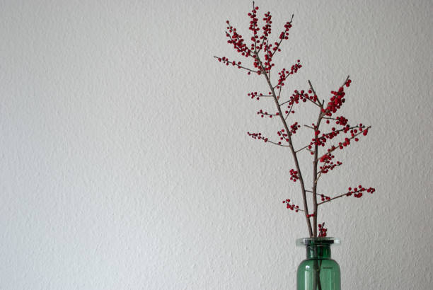 istock Green vase with winterberry branches on a white wall background 1085868040