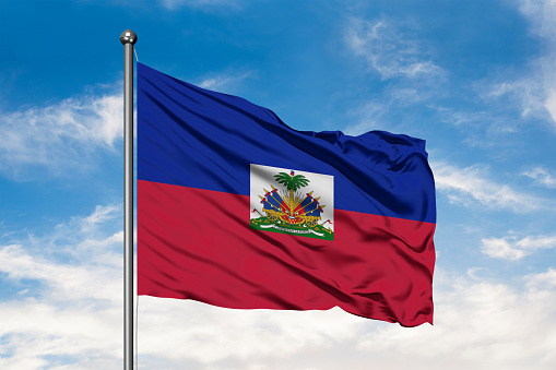 Flag of Haiti waving in the wind against white cloudy blue sky. Haitian flag.