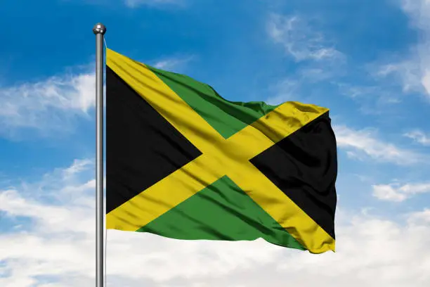 Photo of Flag of Jamaica waving in the wind against white cloudy blue sky. Jamaican flag.