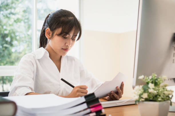 istock Asian Business woman offices check working for stack of unfinishedd documents papers on computer in busy office. Ideas for seaching paperwork and Accounting planning budget Annual report file concept 1085877134