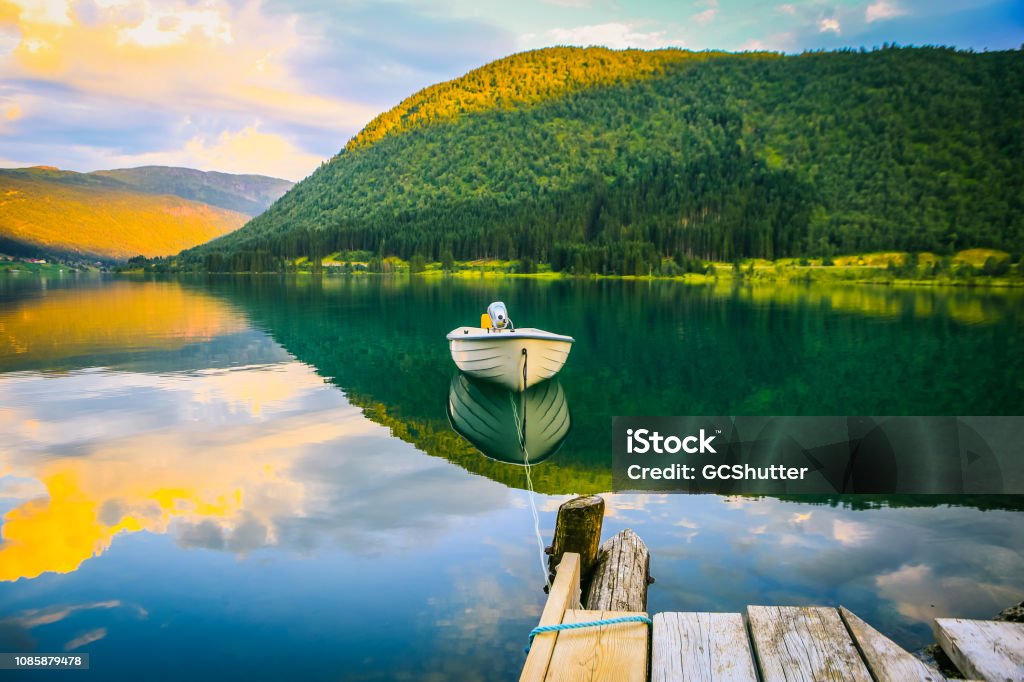 Empty Boat tied to the dock with a rope on the Calm Fjord Fjords, Nature, Landscape - Serene Fjords and Empty Boat tied to the dock against the lush mountain range background. Norway Stock Photo