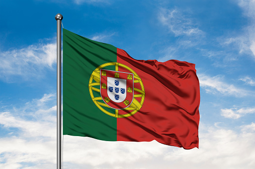 Flag of Portugal waving in the wind against white cloudy blue sky. Portuguese flag.