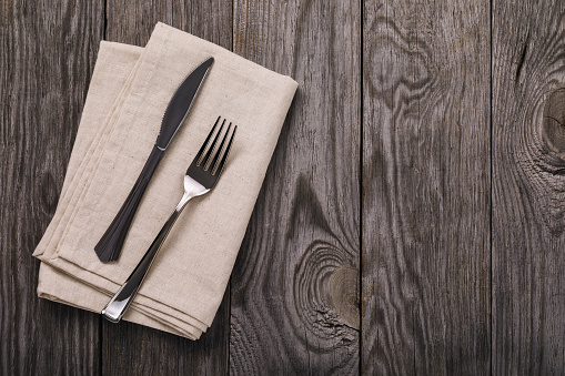 Cutlery and napkin on a wooden table with copy space, top view. Food background
