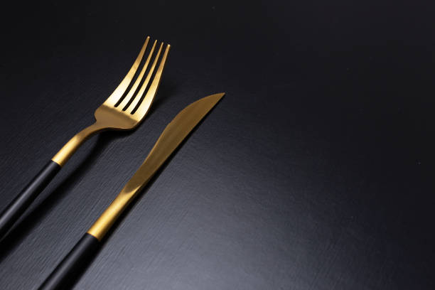 set di posate nere e dore su sfondo nero - table knife silverware black fork foto e immagini stock