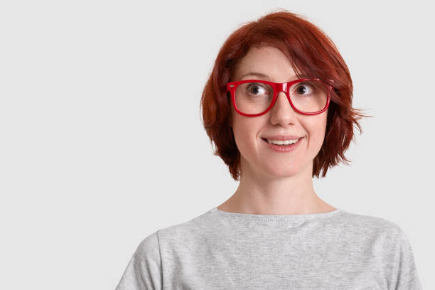 istock Dreamy foxy woman has gentle smile, wears optical glasses, focused upside, dressed casually, models over white background with copy space for your advertisement or promotion. Dreams concept. 1085919364