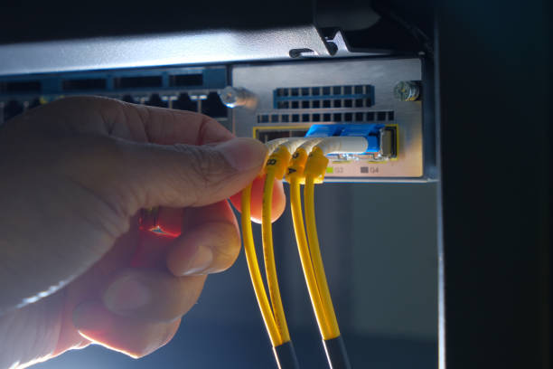 Hand of system engineer and fiber optic cable connected to network router switch in a technology data center room stock photo