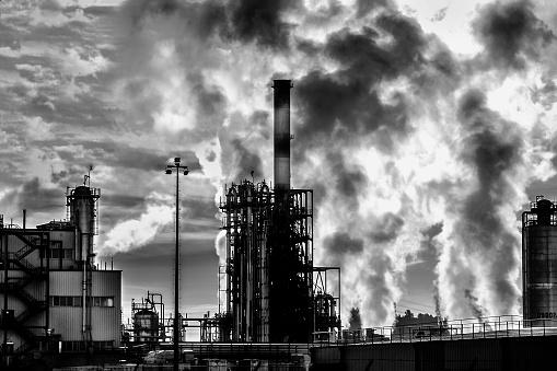 Exterior view of the petrochemical plant in Berre (south of France).
In the foreground, a chimney of the factory.
Huge clouds of smoke come out of the chimneys in the background
On the left, the image opens onto a factory building.
It closes on the right on a tank.
Black and white image