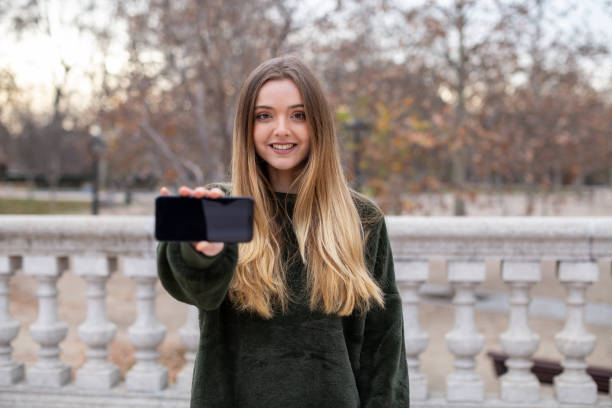 istock Smiling woman showing smartphone in park 1085957268