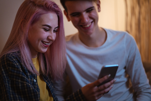 Smiling teenagers are surfing the net on smart phone at home.
