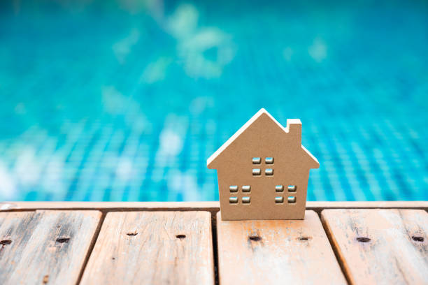 Wooden house model on the deck of swimming pool. Concept for property ladder, mortgage and real estate investment . stock photo