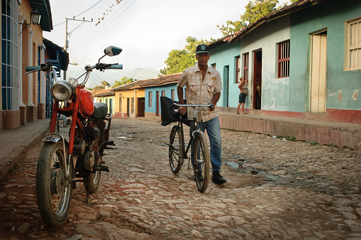 Man passing by with his bicycle, and a vintage motorbike, on the cobbled streets of Trinidad, Cuba