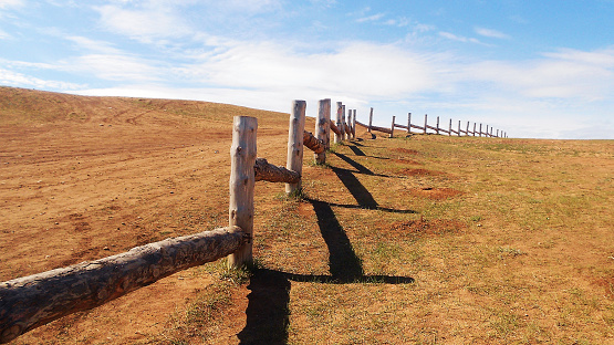 Beautiful summer landscape of pasture for cattle. Wooden fence in prairie, blue sky with clouds. Separation barrier of agricultural land in steppe.