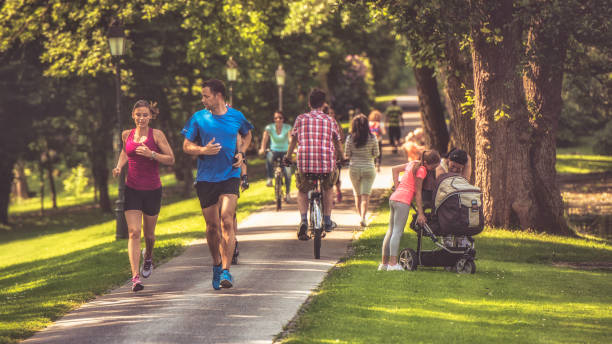 Couple jogging in the park Couple jogging through a busy park on a sunny day. People cycling and walking and a woman and girl looking at a baby in a baby carriage. public park stock pictures, royalty-free photos & images