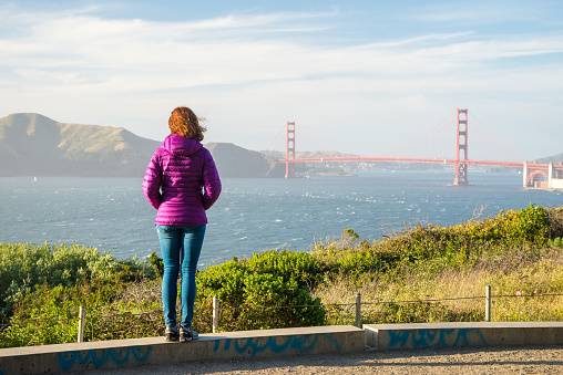 Young woman is watching Golden Gate bridge from Baker Beach in San Francisco, United States on America