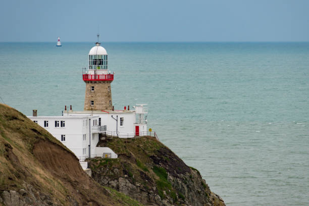 Baily Lighthouse, Dublin, Ireland - December 16 2018: View of The Baily Lighthouse on the Howth peninsula cliffs with a second illuminated lighthouse in the Irish Sea in the background. Copy space.