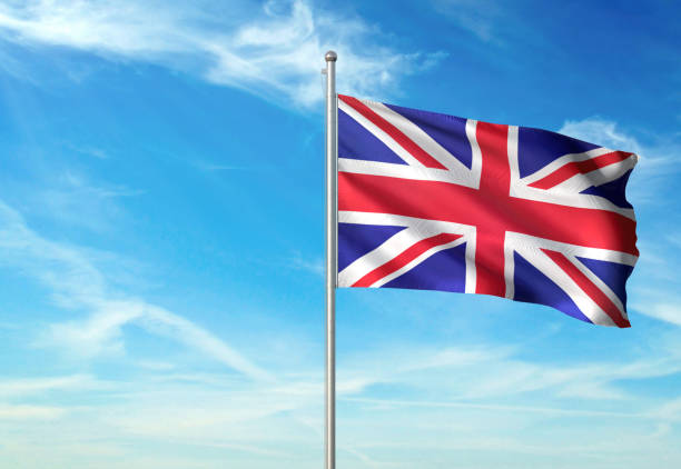 Bright Union Jack flag flying on white flag pole in blue sky