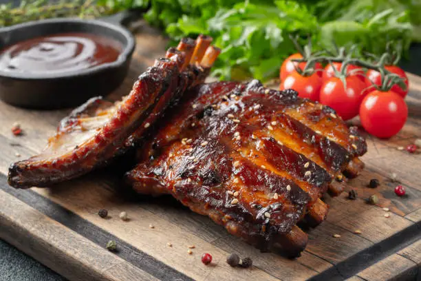 Photo of Closeup of pork ribs grilled with BBQ sauce and caramelized in honey. Tasty snack to beer on a wooden Board for filing on dark concrete background