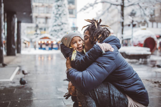 Young father with daughter walking on snowy street and enjoy in winter magic. They wearing warm clothing