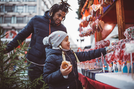Young father with daughter on Christmas market. They walking around and picking what to buy.