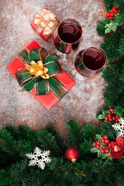 istock Red wine in glasses prepared with present boxes on snow wood board, pine branches and Christmas ornaments border decorate top view 1086163100
