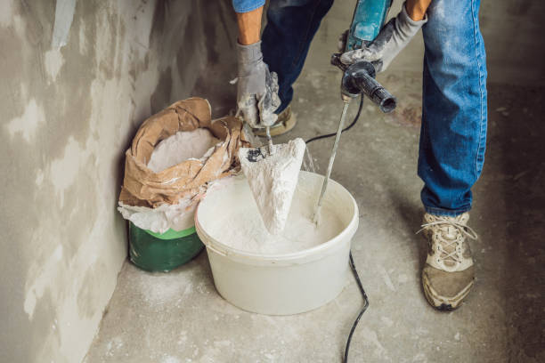 istock Young male painter kneads putty with water in a bucket using a hand-held mixer for building mixes 1086182956