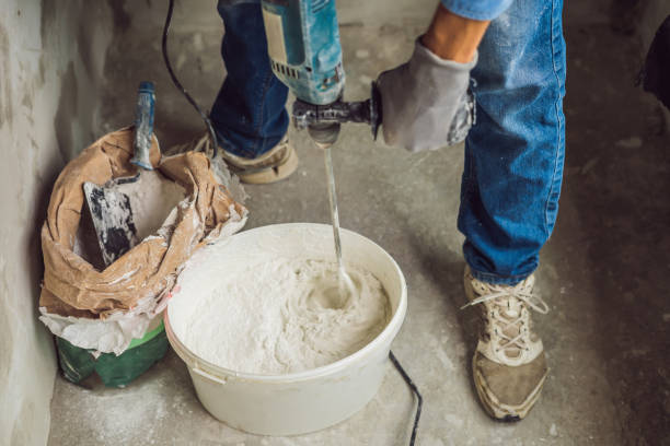 istock Young male painter kneads putty with water in a bucket using a hand-held mixer for building mixes 1086182970