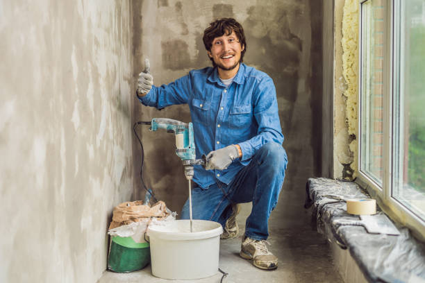 Young male painter kneads putty with water in a bucket using a hand-held mixer for building mixes