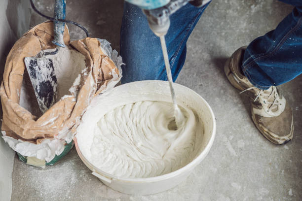 istock Young male painter kneads putty with water in a bucket using a hand-held mixer for building mixes 1086182984