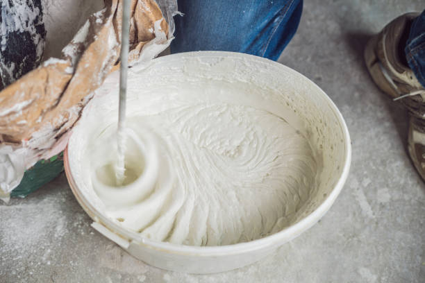 istock Young male painter kneads putty with water in a bucket using a hand-held mixer for building mixes 1086182986